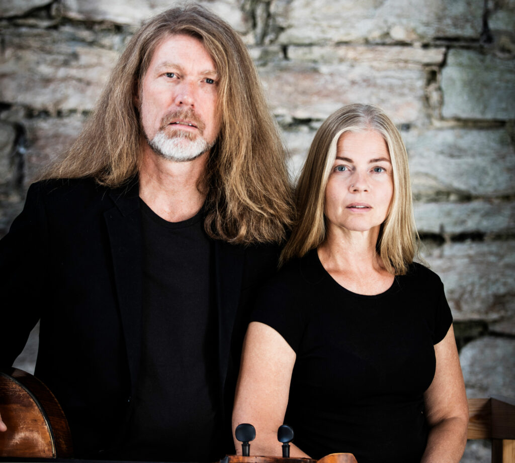 Porträtt av Katarina och Svante Henryson i svarta kläder mot tegelvägg.