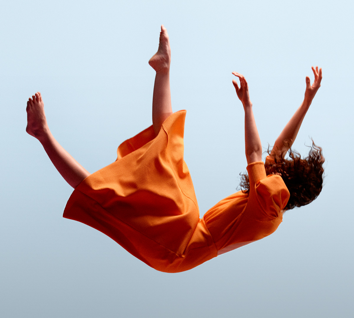 En kvinna i orange klänning faller mot en ljusblå bakgrund.