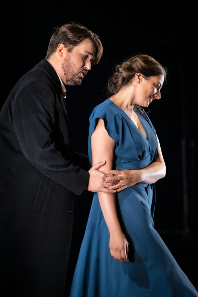 Den unge mannen i svart kostym håller om armen på den unga leende kvinnan i blå klänning.