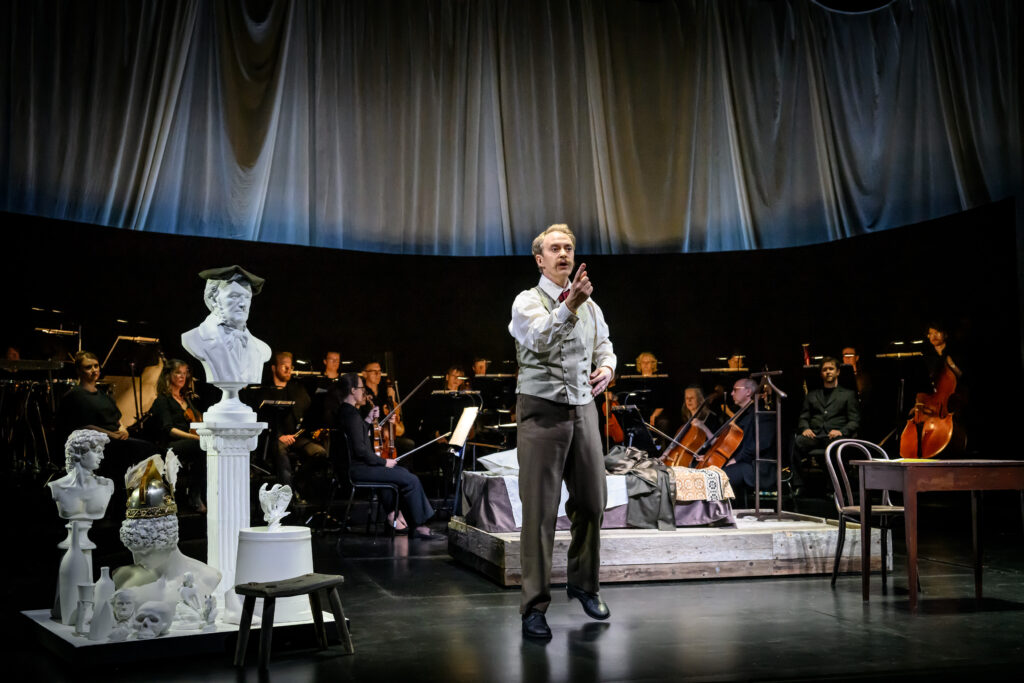 Jonas Karlsson som Nietzsche som Nietzsche på scen med Folkoperans orkester och en byst av Wagner.