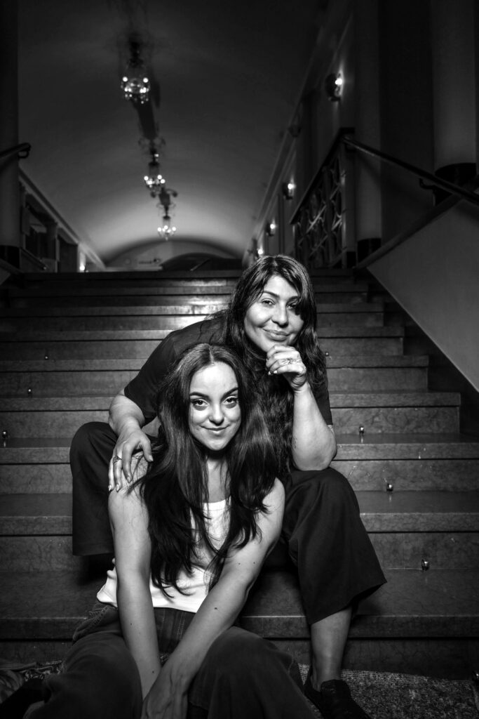Nina Rashid och Bahar Pars sitter tillsammans i en stentrappa inne i Folkoperans foajé.